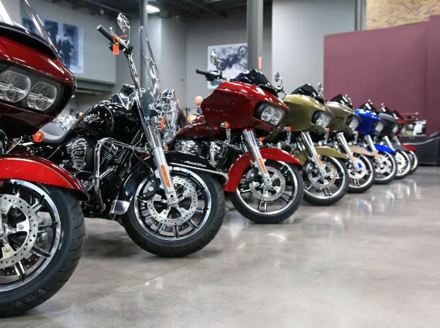 A row of various colored touring motorcycles parked indoors on a polished floor, with front wheels turned slightly to the left, in a showroom or exhibition hall.