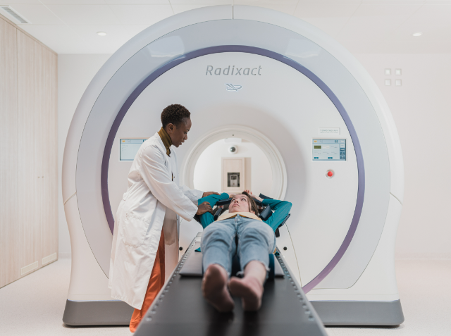 A healthcare professional adjusts the head support for a patient lying on a Radixact medical imaging treatment table in a clinical setting.