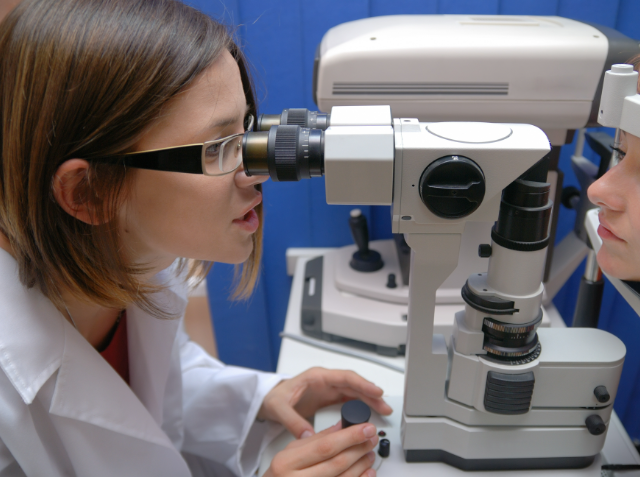 An optometrist using a slit lamp to examine a patient's eye in a clinical setting.