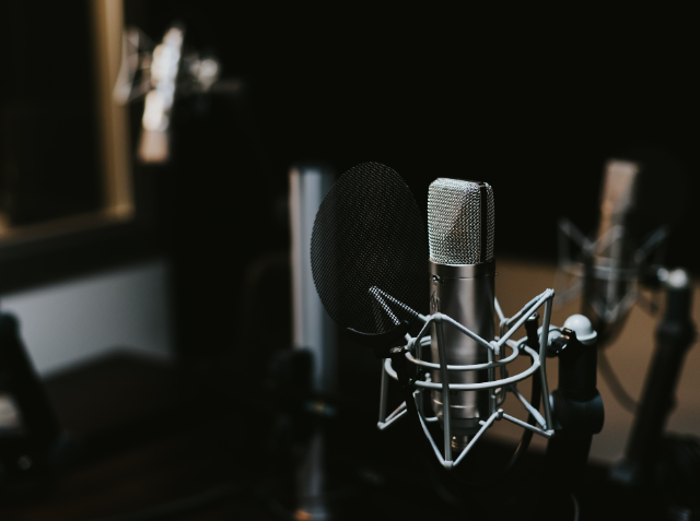 Professional studio microphone with pop filter on a stand, with additional microphone stands in the blurred background, indicative of a recording studio.