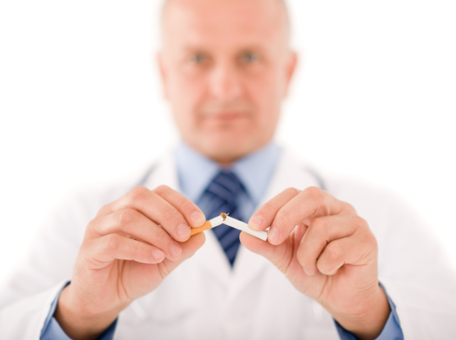 A doctor in a white coat and tie breaking a cigarette in half, symbolizing smoking cessation.