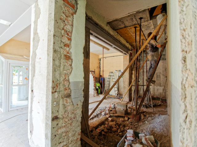 Interior construction site with scattered debris, a worker on scaffolding, and renovation in progress.