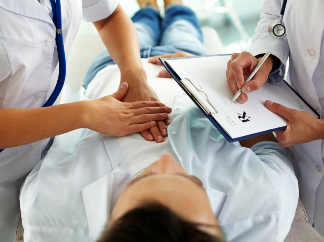 A healthcare professional comforting a patient by holding their hand while another professional takes notes on a clipboard during a medical consultation.