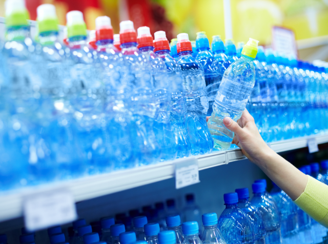 A person's hand picking a bottle of water from a shelf stocked with various bottled waters with colorful caps.