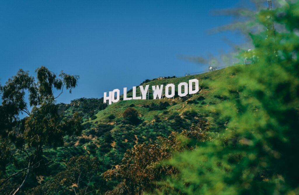 The Hollywood sign on a sunny day, set against a clear blue sky with green hills in the foreground.