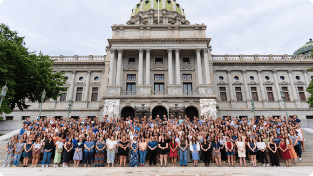 A diverse group of people posing on the steps of a grand government building with a dome and columns.