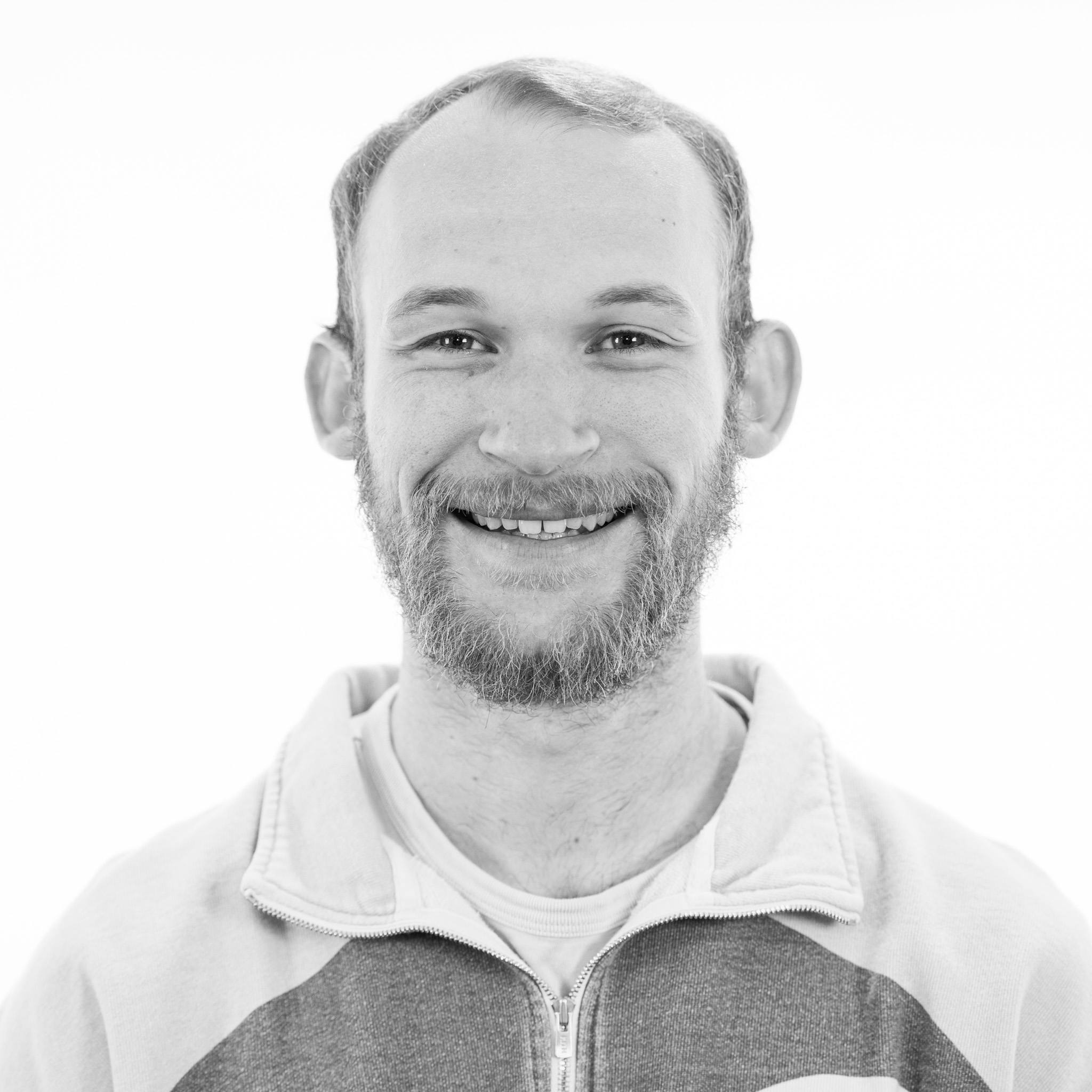 Black and white portrait of a smiling man with a beard, wearing a hoodie.