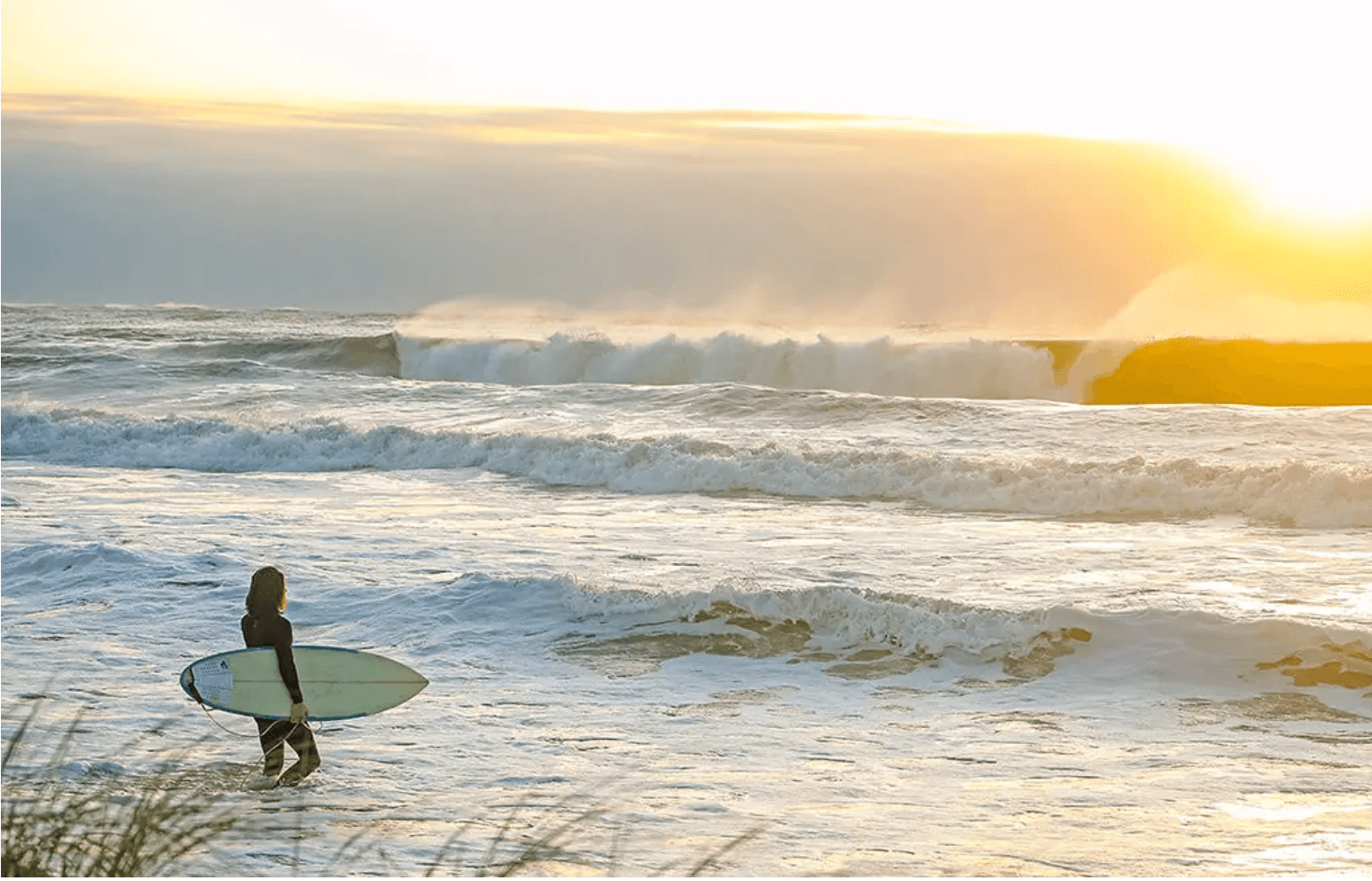 Man with a surfboard standing in the ocean at sunrise