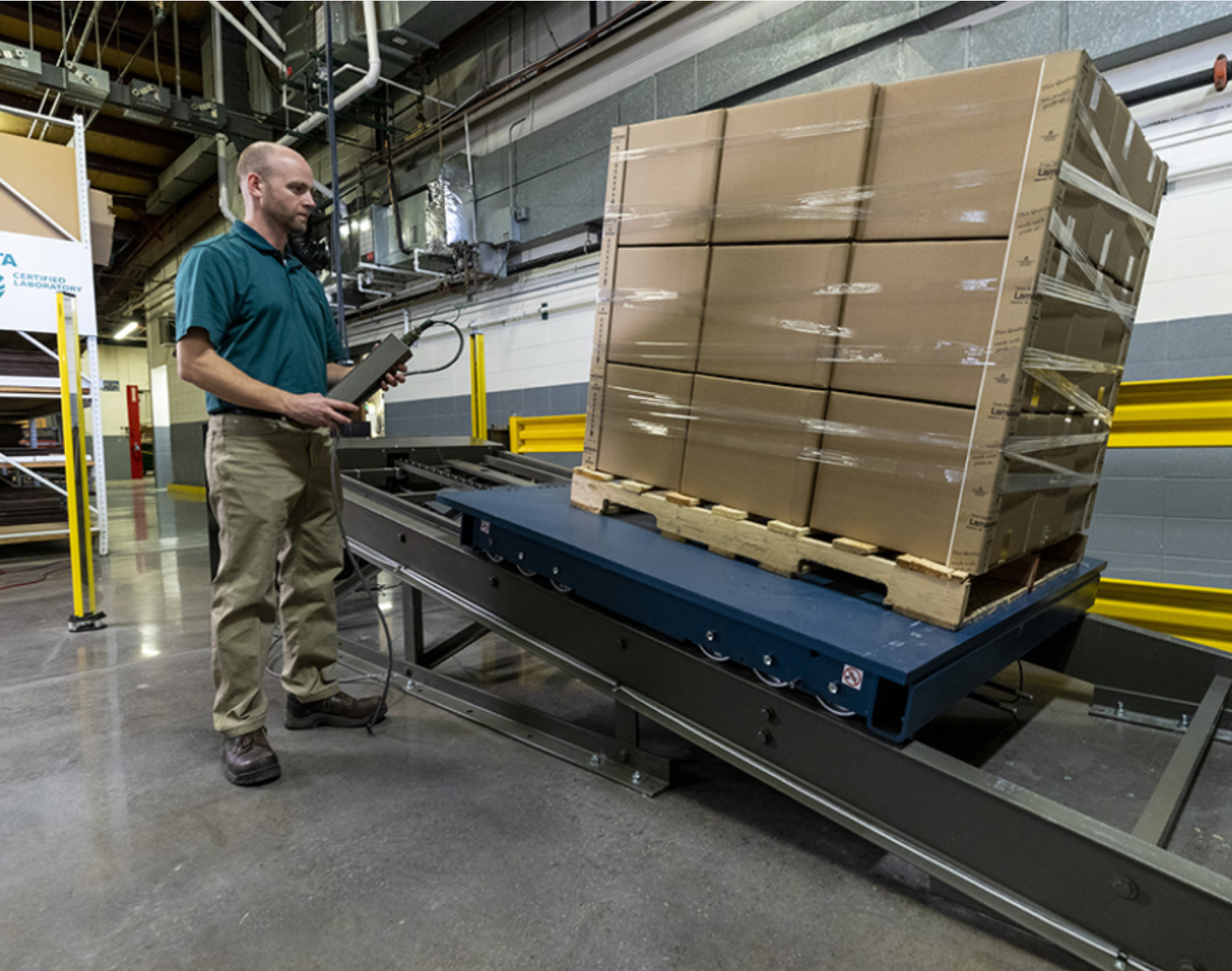 Man in a teal polo lifting a pallet of boxes