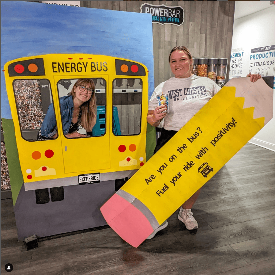 Two girl posing with a giant pencil sign and school bus cutout