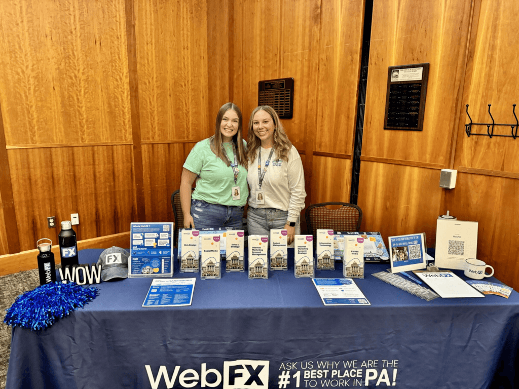 Julie and Emily standing in front of a WebFX table at a career fair
