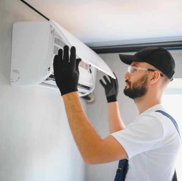 A technician in gloves and glasses installs an air conditioning unit on a wall