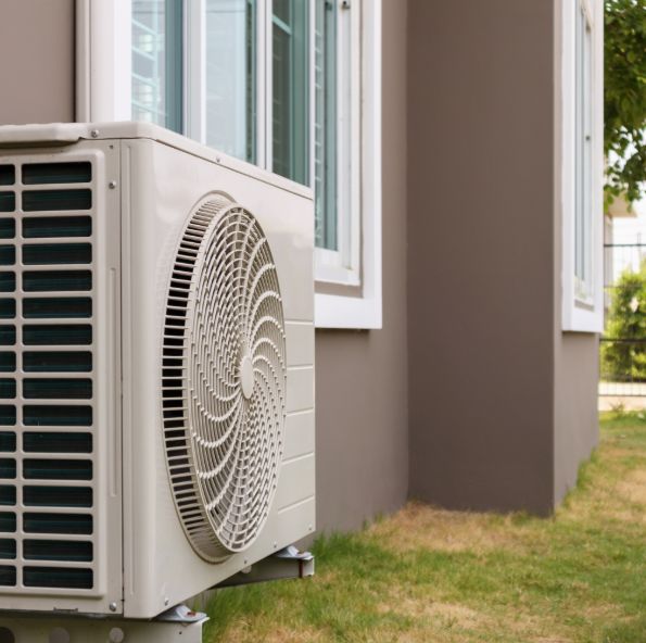 An outdoor air conditioning unit installed beside a house, with grass and a fence in the background