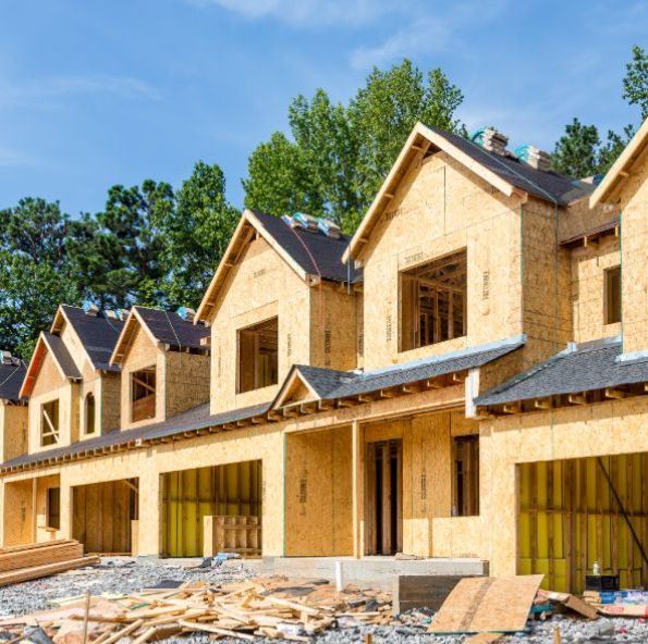 Several new homes under construction, featuring wooden frames and open windows, surrounded by building materials and trees