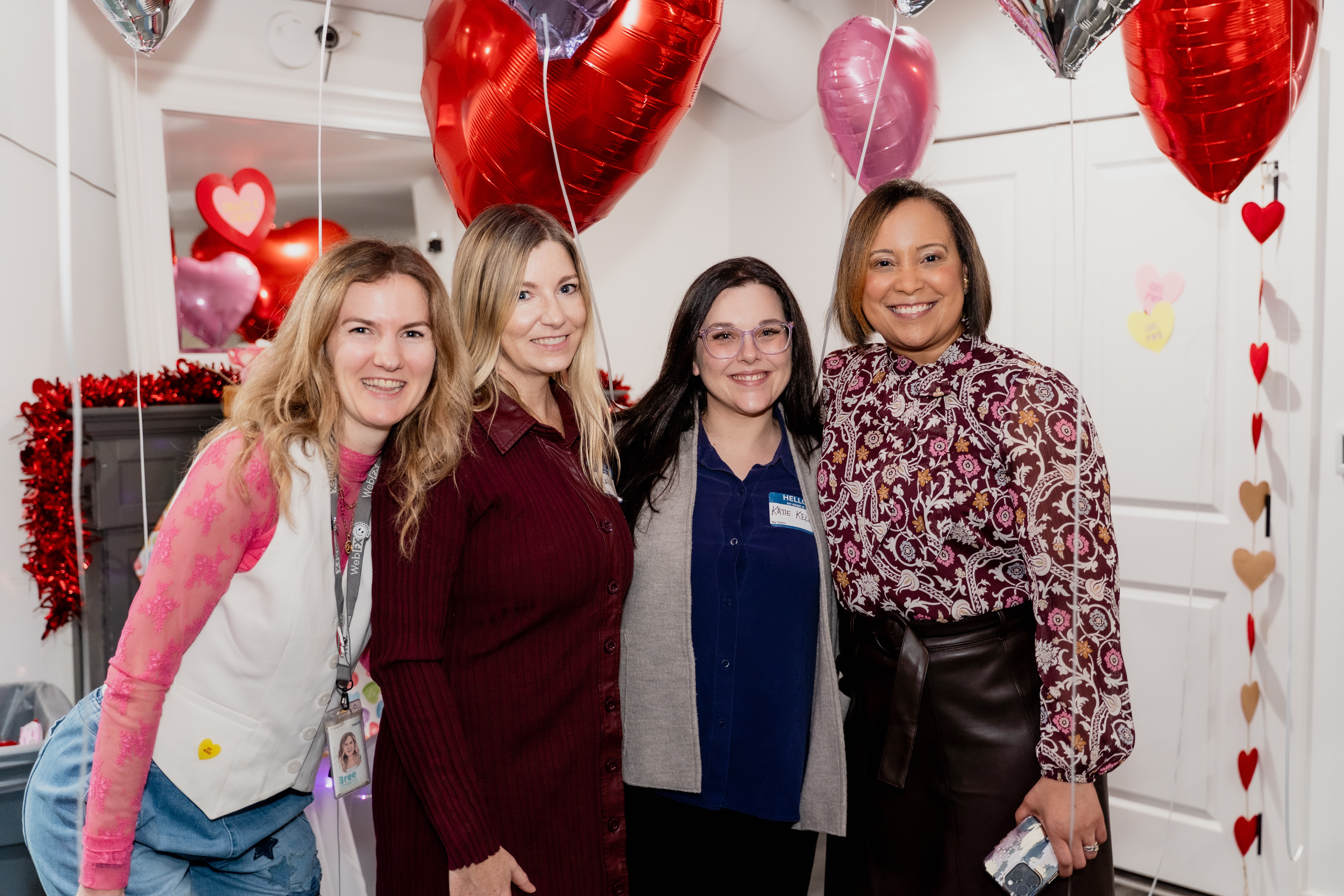Four women posing for a photo with heart balloons in the background