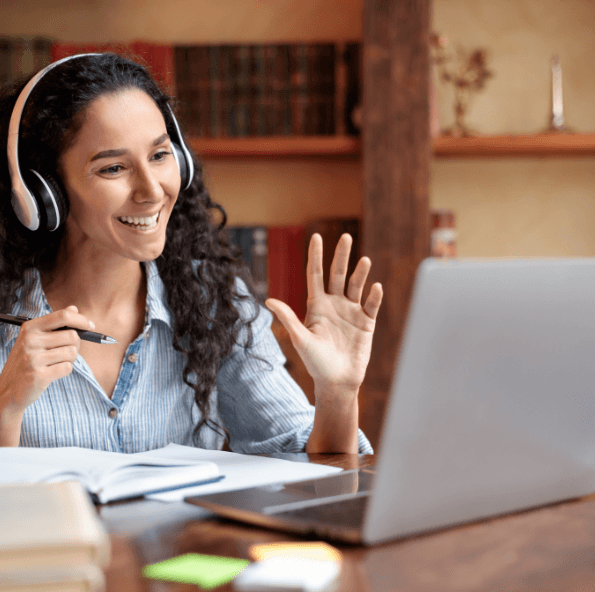 Smiling woman wearing headphones waving at laptop camera during virtual class session