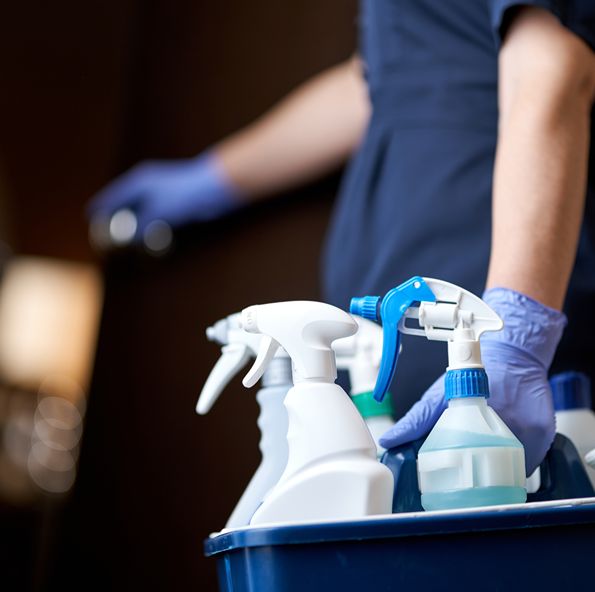 Gloved hand reaching into a cleaning caddy of spray bottles
