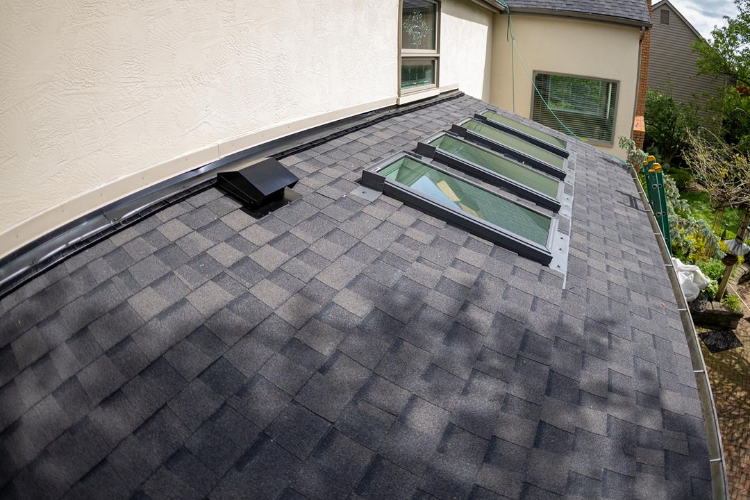 Gray asphalt shingle roof with four skylights and a black roof vent
